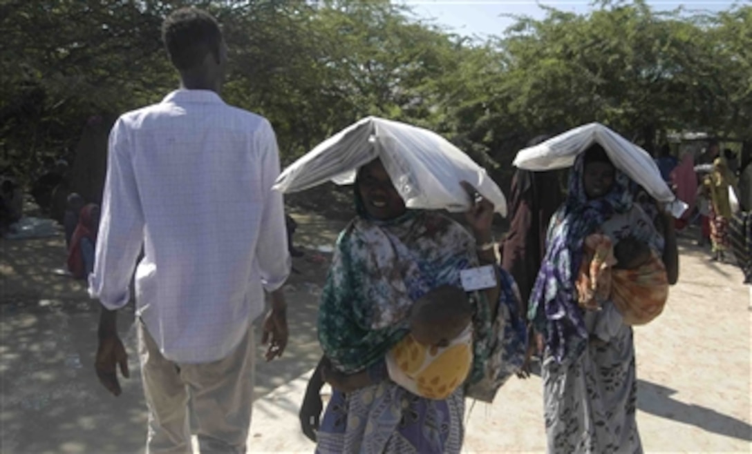 Victims of recent severe flooding  in Dadaab, Kenya, leave a distribution center in one of three refugee camps with tarps received from the CARE distribution center at the Ifo camp, Dec. 12. These tarps, as well as mosquito nets, were part of bundles air-dropped into the area over the past week by aircraft from the Combined Joint Task Force -- Horn of Africa. 