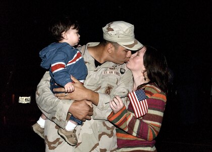 While holding his 13-month-old son, Gabriel, Staff Sgt. Matthew Rodriguez, 37th Security Forces Squadron, receives a loving "welcome home" kiss from his wife, Polly Rodriguez. Sergeant Rodriguez returned home from a six-month deployment Sunday evening with more than 110 other Airmen from across the Air Force. (Photo by Alan Boedeker)                               