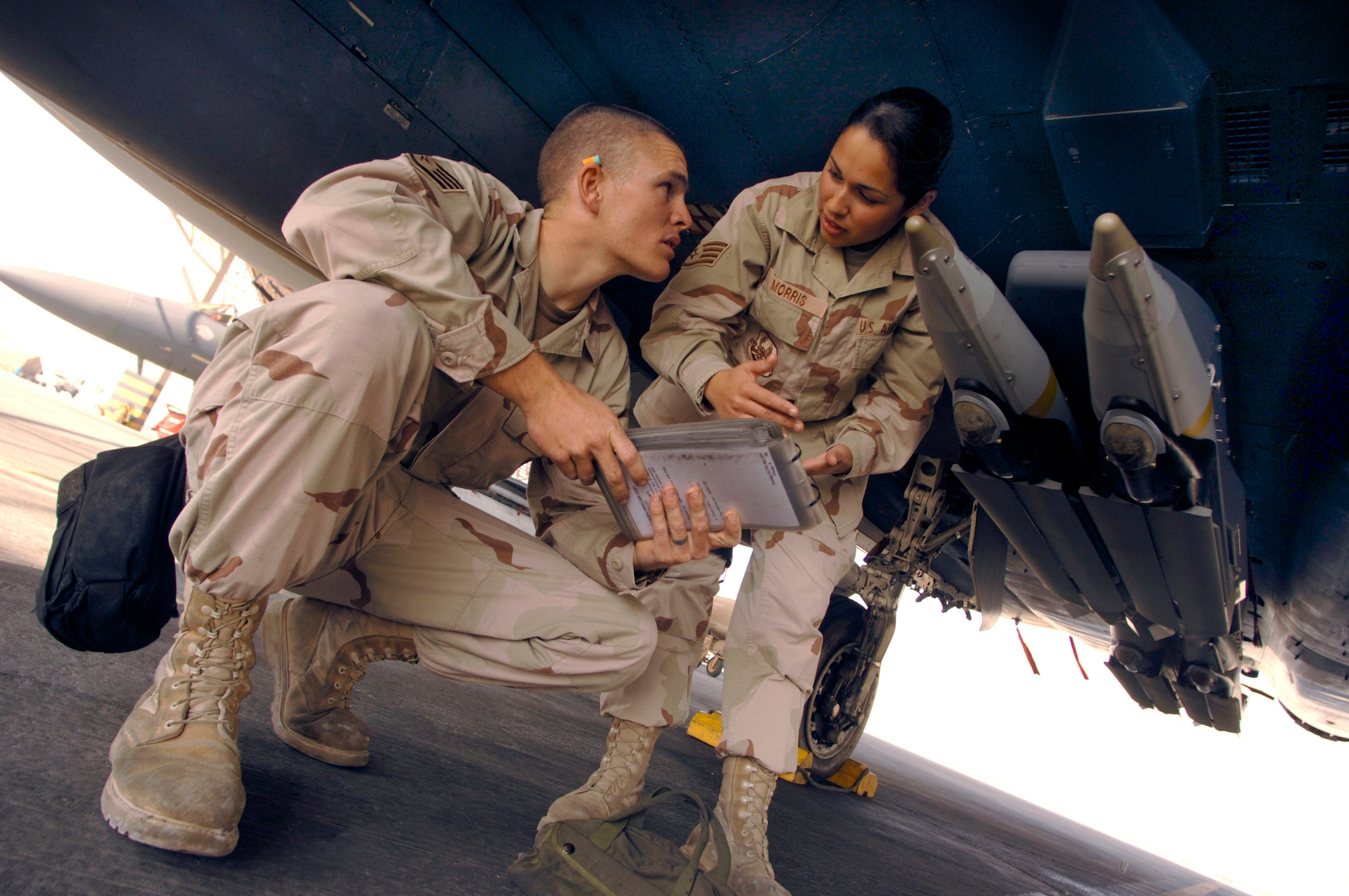 Staff Sergeants Chace and Maria Morris go over a technical order under an F-15E Strike Eagle Dec. 9 on the flightline at a forward-operating base in Southwest Asia. They have been married more than four years and are both deployed together supporting the war on terrorism. (U.S. Air Force photo/Master Sgt. Scott Wagers) 