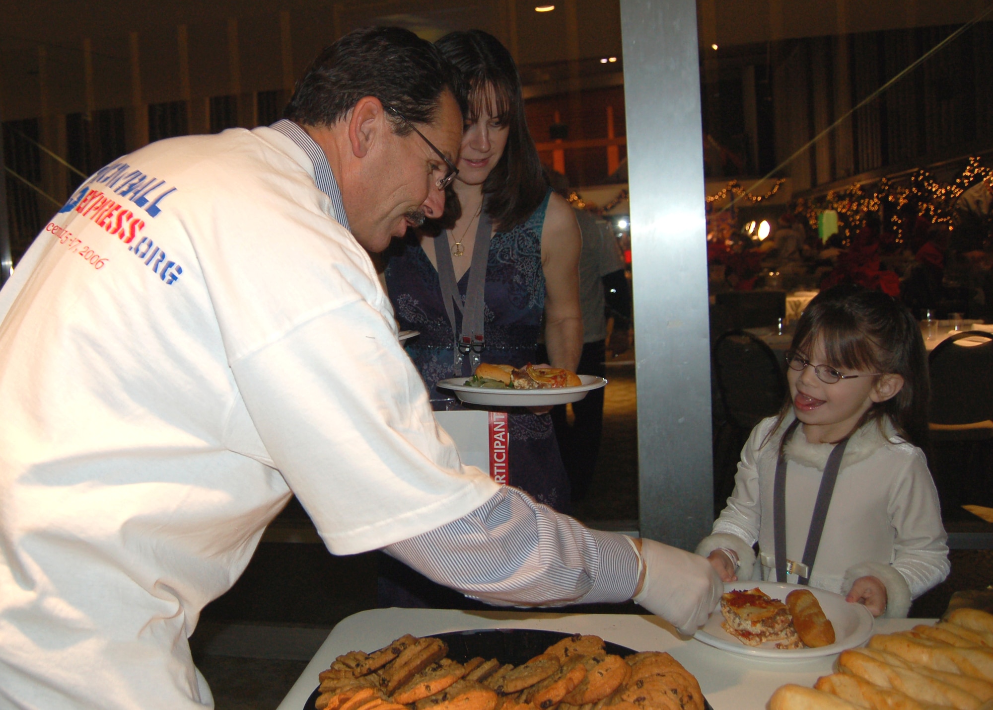 Dave Rudat, a Snowball Express volunteer, hands a cookie to Lauren Stubenhofer as her mom Lauren looks on Dec. 15 at the Crystal Cathedral. The dinner was the first activity of the four-day event. The Snowball Express includes a trip to Disneyland and tickets to an Anaheim Ducks game. (U.S. Air Force photo/Staff Sgt. Jeremy Larlee) 