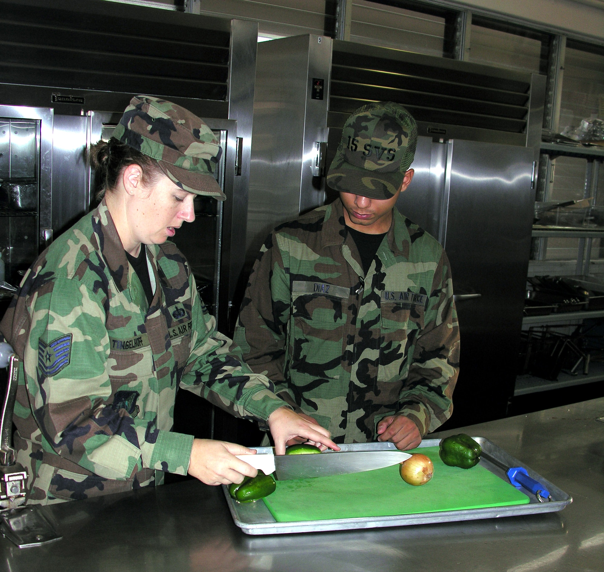 Tech. Sgt. Regan Tingelhoff shows Airman Basic Alex Diaz how to chop vegetables for the lunch meal. Airman Diaz will work this Christmas at the Hale' Aina Dining Facility at Hickam Air Force Base, Hawaii. (U.S. Air Force photo/Senior Airman Erin Smith)

