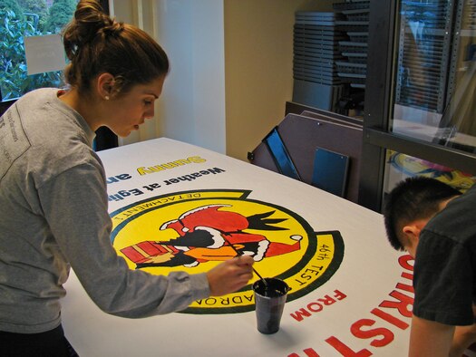 From left, 2nd Lt. Miriam Coleman and 1st Lt. Mu Jin Kim, 46th Test Squadron Detachment 1, apply the finishing touches on their unit's holiday card for the Hanscom Holiday Card Competition Dec. 14. Judges will choose first, second and third place winners Dec. 21. (U.S. Air Force photo by 2nd Lt. Brian P. Donnell)
