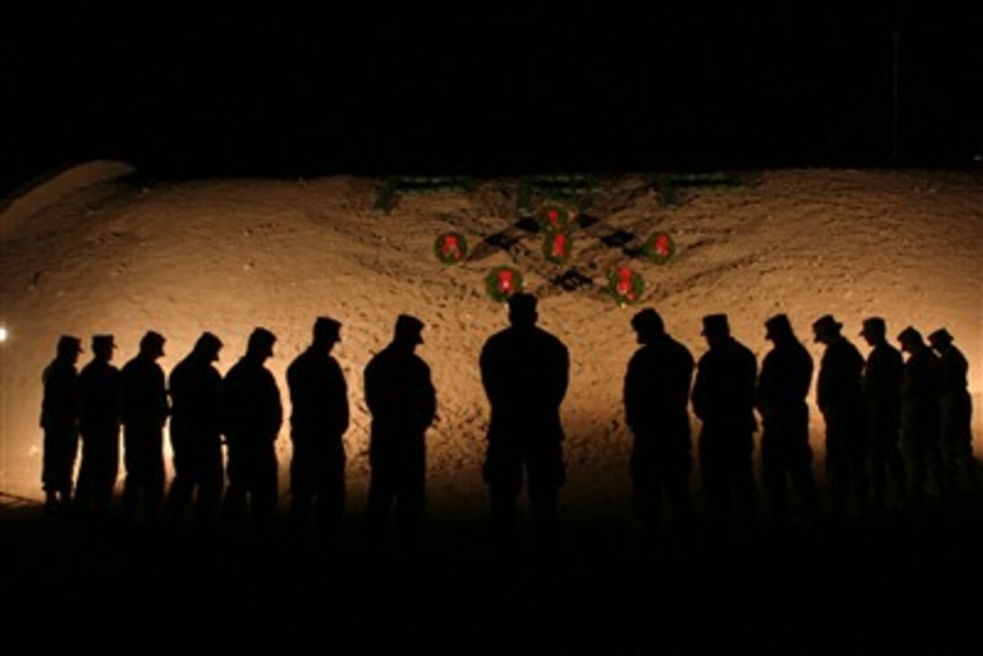 U.S. Marines with 1st Marine Logistics Group (Forward) bow their heads in silence in honor of fallen comrades during an evening vigil at Camp Al Taqaddum, Iraq, on Dec. 14, 2006.  The holiday wreaths are a donation from the Worcester Wreath Company as part of an expansion of the 15-year old tradition known as the Arlington Wreath Project, in which thousands of holiday wreaths are brought to Arlington Cemetery in Arlington, Va., to adorn headstones.  The vigil is being timed to coincide with a similar ceremony being held in Arlington National Cemetery.  