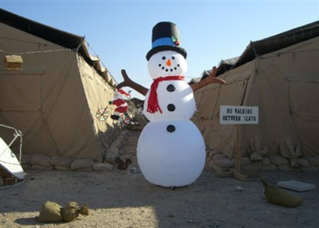 Servicemembers at Camp Navistar, Kuwait, get into the holiday spirit as a snowman stands guard between the tents and Santa cllimbs the canvas wall.