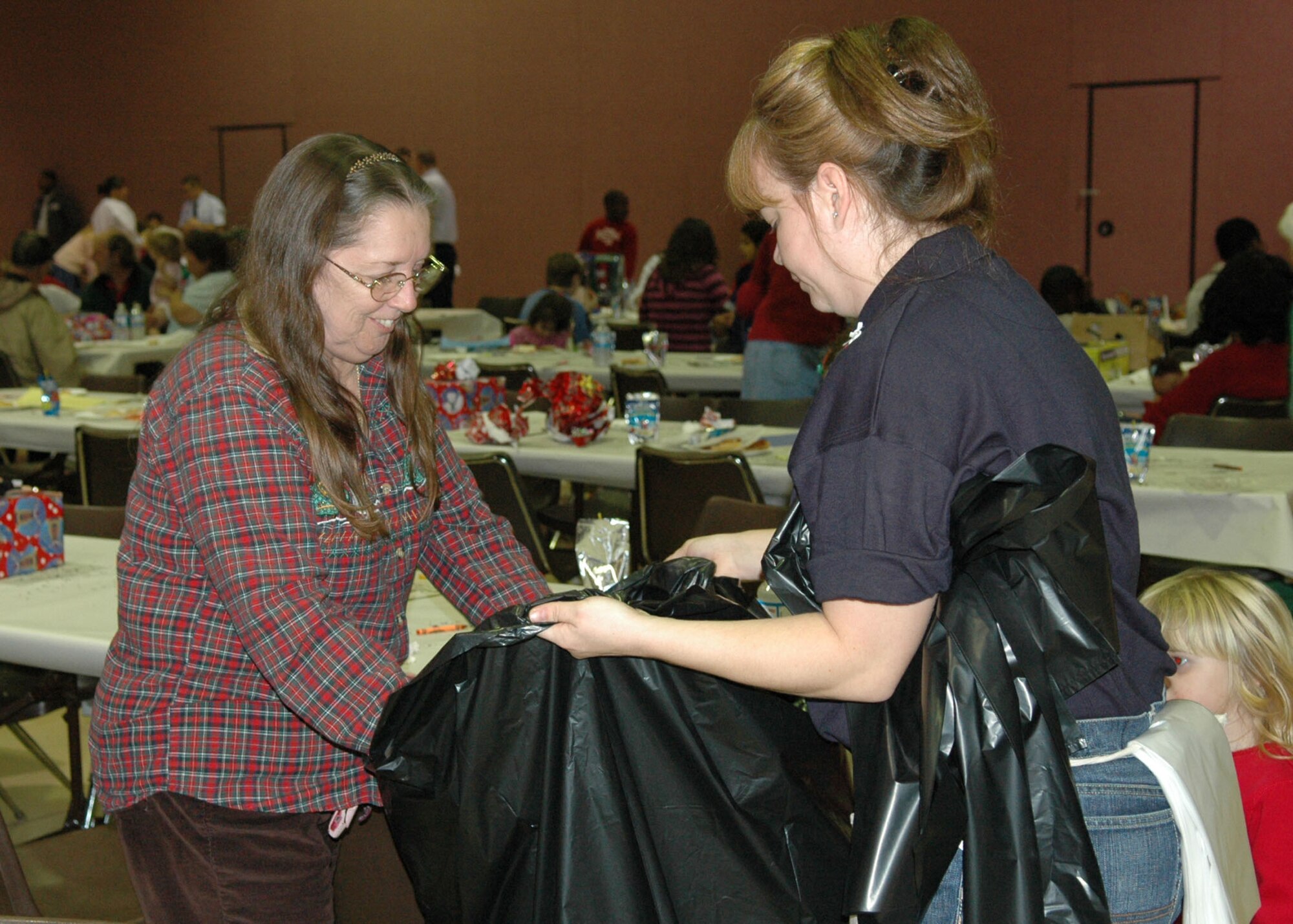 Rachell Wood (right), a technical sergeant and 917th Wing Financial Management technician, holds a bag open for a lady whose children were gift recipients at this year's Santas in Blue program held at the Bossier Civic Center, Bossier City, Thursday, Dec. 21. The 917th Wing donated approximately 300 gifts to the program, which gives gifts to needy children each year. 