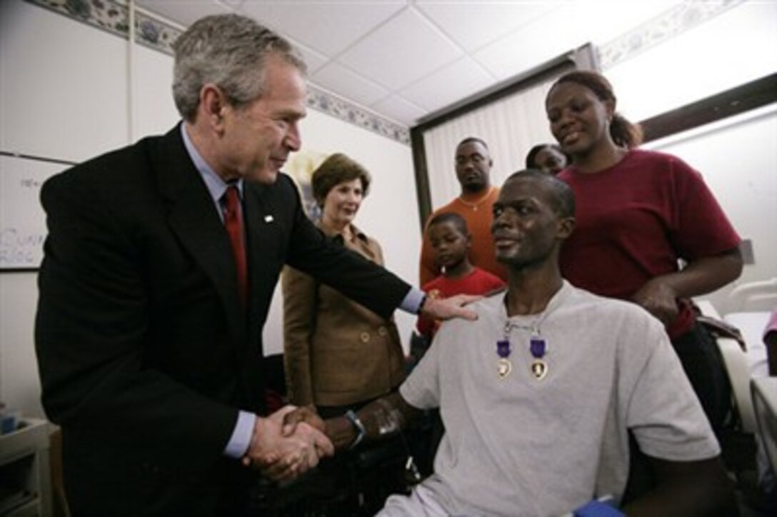 President George W. Bush shakes the hand of Staff Sgt. Marcus Wilson after awarding him two Purple Hearts at the Walter Reed Army Medical Center in Washington, D.C., Dec. 22, 2006, as Laura Bush and members of the Marine's family look on. Wilson, who is from Dermott, Arkansas, is recovering from wounds suffered in Operation Iraqi Freedom.