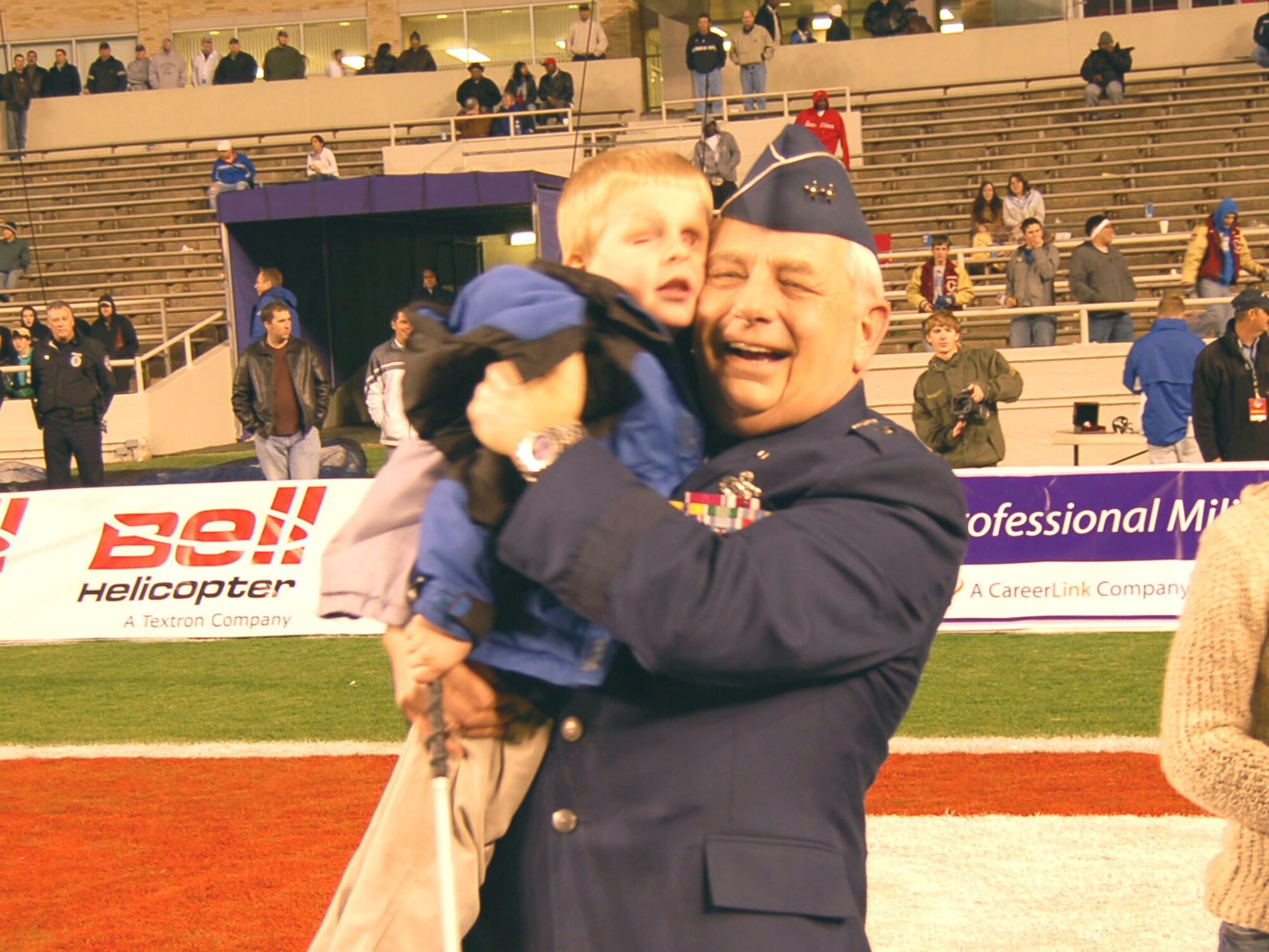 Maj. Gen. Allen R. Dehnert, assistant adjutant general and commander, Texas Air National Guard, hugs 5-year-old Sawyer Deevers, a boy with vision impairment from Iowa. Sawyer has been a big contributor to Connect and Join, and has sent messages of support written in Braille to servicemembers deployed overseas. Sawyer's pages were part of several scrapbooks presented to the general to send to the troops overseas. The presentation was part of the Bell Helicopter Armed Forces Bowl in Fort Worth, Texas, Dec. 23. (U.S. Air Force photo/Annette Crawford)