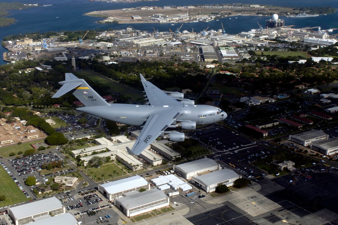 HICKAM AIR FORCE BASE, HAWAII (AFPN) -- The first Hawaii-based C-17 Globemaster III flies over Hickam Air Force Base and nearby Pearl Harbor for the arrival ceremony. Hickam is the first base outside the continental U.S. to permanently host the C-17. By the end of the year, the base will be home to eight C-17s. The 15th Airlift Wing and the Hawaii Air National Guard 154th Wing will jointly operate and maintain the aircraft. (U.S. Air Force photo by Tech. Sgt. Shane A. Cuomo) 