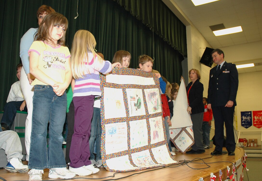 First-grade children at Sangree Elementary School in Summerville, S.C. present "Quilts of Valor" to Chaplain (Maj.) John Painter (right), a reservist assigned to the 315th Airlift Wing at Charleston AFB, S.C.  Chaplain Painter accepted two quilts on behalf of his civilian employer the Ralph H. Johnson VA Medical Center and two quilts that will be delivered by the 315th Airlift Wing to a regional hospital in Germany. (Photo by Tech. Sgt. Mark Kleber)