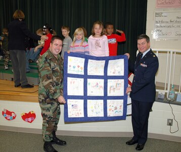 First-grade children at Sangree Elementary School in Summerville, S.C. present "Quilts of Valor" to Chaplain (Maj.) John Painter (right) and 1st Lt Wayne Capps (left), reservists assigned to the 315th Airlift Wing at Charleston AFB, S.C.  Chaplain Painter accepted two quilts on behalf of his civilian employer the Ralph H. Johnson VA Medical Center and two quilts that will be delivered by the 315th Airlift Wing to a regional hospital in Germany. (Photo by Tech. Sgt. Mark Kleber, USAFR)