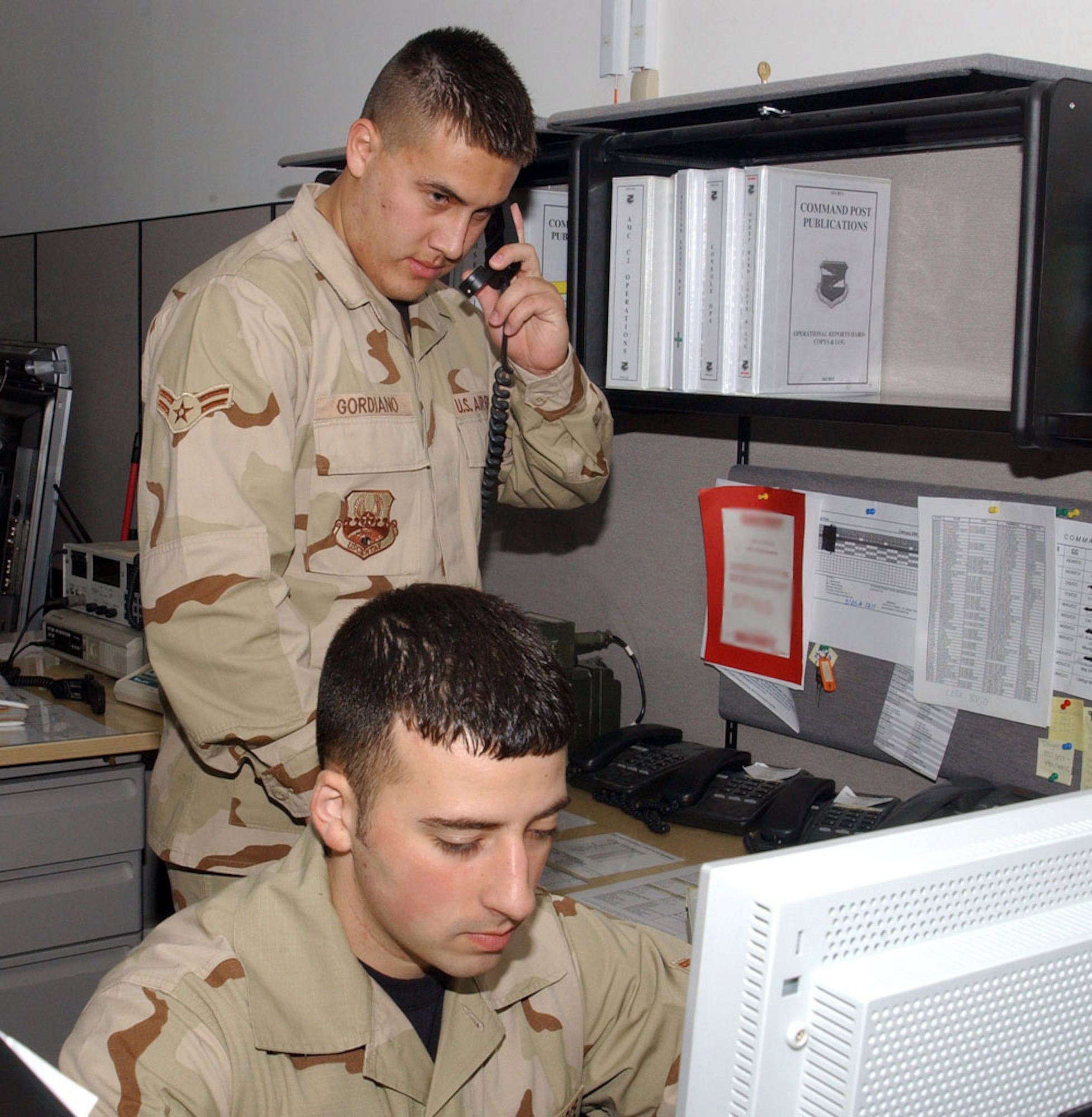 SOUTHWEST ASIA (AFPN) -- Airmen 1st Class Ali Saffarini and Jeremiah Gordiano (standing) work together to input an event during a recent night-shift turnover. They are 380th Air Expeditionary Wing command post controllers, and are a vital link in the flow of information to the wing commander from base agencies. (U.S. Air Force photo by Tech. Sgt. Andrew Leonhard) 

        