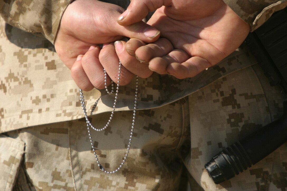 A Marine from Charlie Company, Battalion Landing Team 1st Bn., 2nd Marines, the ground combat element of the 22nd Marine Expeditionary Unit (Special Operations Capable), holds a pair of dog tags during a memorial service held at Al Asad Air Base, Iraq Feb. 18, 2006.  Cpl. Orville Gerena, Lance Cpl. David Parr, and PFC Jacob Spann of Charlie Company were killed conducting counterinsurgency operations in Iraq's Al Anbar province.::n::