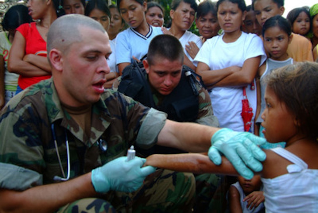 Navy Hospital Corpsman Eric Schaefer treats a Filipina girl as a crowd gathers around to watch in the small fishing village of Himbangan, Philippines, on Feb. 22, 2006. Sailors and Marines from the amphibious assault ship USS Essex (LHD 2) and the dock landing ship USS Harpers Ferry (LSD 49) are providing humanitarian assistance for the victims of the Feb. 17, 2006, landslide in the village of Guinsaugon on the island of Leyte. 