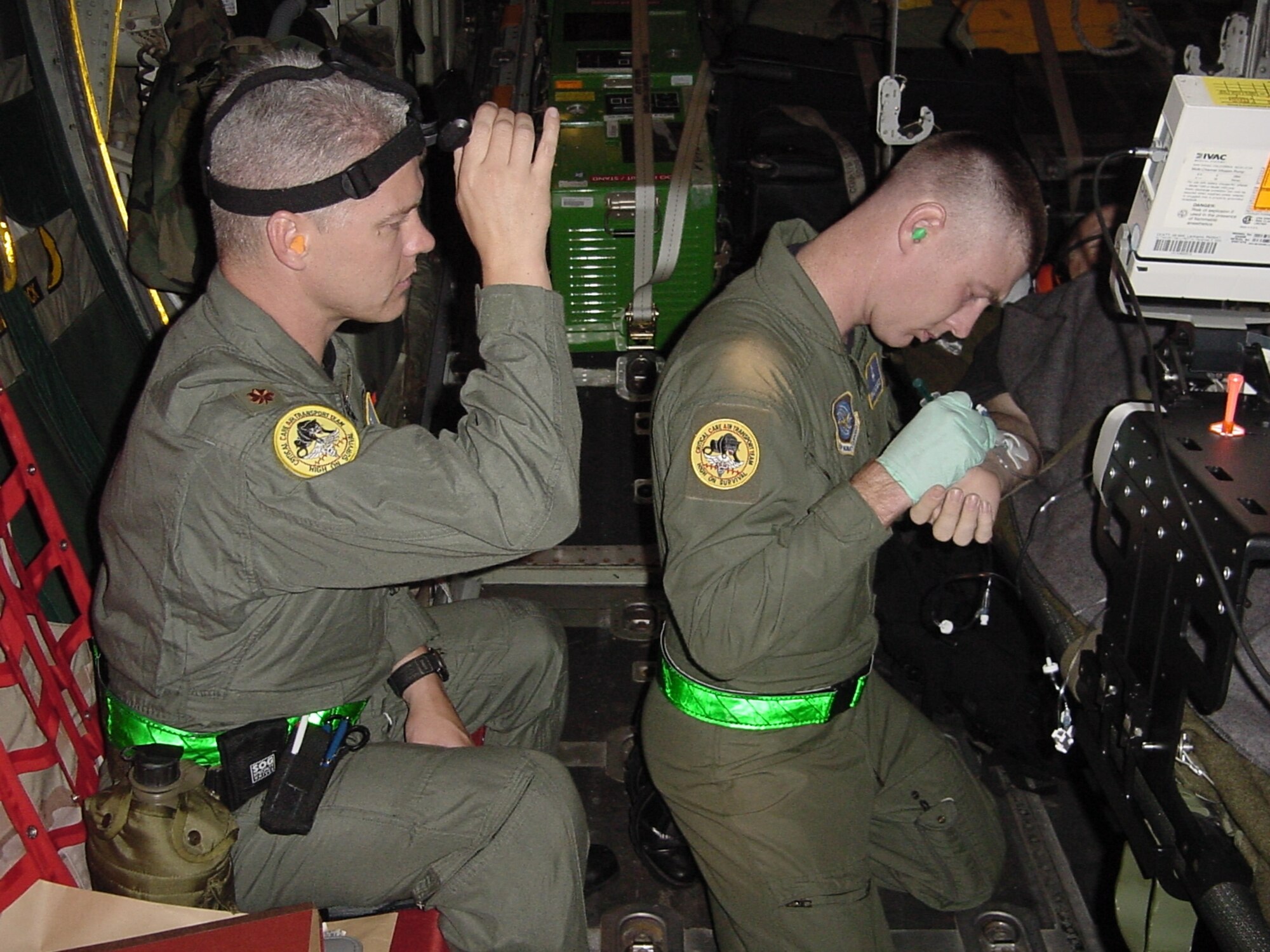 Critical Care Air Transport Team nurse Maj. Rodney Logan, 60th Medical Operations Squadron, sheds a little light for Tech. Sgt. William Webster, a cardiopulmonary CCATT member, as he administers to a Hurricane Katrina evacuee during an aeromedical evacuation mission aboard a C-130 Hercules in September 2005. (U.S. Air Force photo by Dr. [Maj.] Lazaro Bravo)