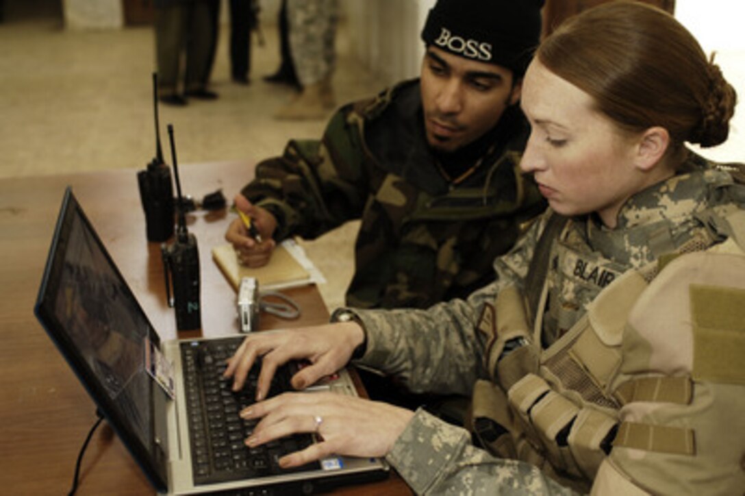 U.S. Army Sgt. Sarah L. Blair enters vital information of Iraqi policemen into a laptop computer as Iraqi aide Antonio translates at an Iraqi police station in Samarra, Iraq, on Feb. 12, 2006. Blair is attached to the 4th Platoon, 987th Military Police Company. 