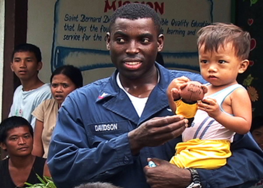 Navy Petty Officer 2nd Class Reginald Davidson gives a toy to one of the survivors of the Feb. 17th landslide in the village of Guinsaugon on the island of Leyte, Philippines, on Feb. 25, 2006. More than 50 sailors and Marines participated in the community relations project from cleaning the schoolhouse where the survivors are staying to handing out donated clothing, toys and food items. Davidson is a Navy aviation structural mechanic aboard the amphibious assault ship USS Essex (LHD 2). 