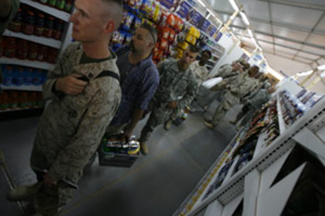 Sergeant John G. Totzke, 22, from Lees Summit, Mo., is next in line as he waits to buy a CD and magazine at the grand opening of Camp Taqaddum's main exchange July 1, 2006. The exchange services here moved their store from a wooden building to a much larger structure to provide their customers with a more open area to shop that stays cooler than the previous location. Service members go to the PX to buy goods ranging from basic hygiene equipment such as toothpaste and razors to luxury items like the latest video game magazine or favorite soft drink; the latter category crucial to Marines fighting in the forefront of Operation Iraqi Freedom.