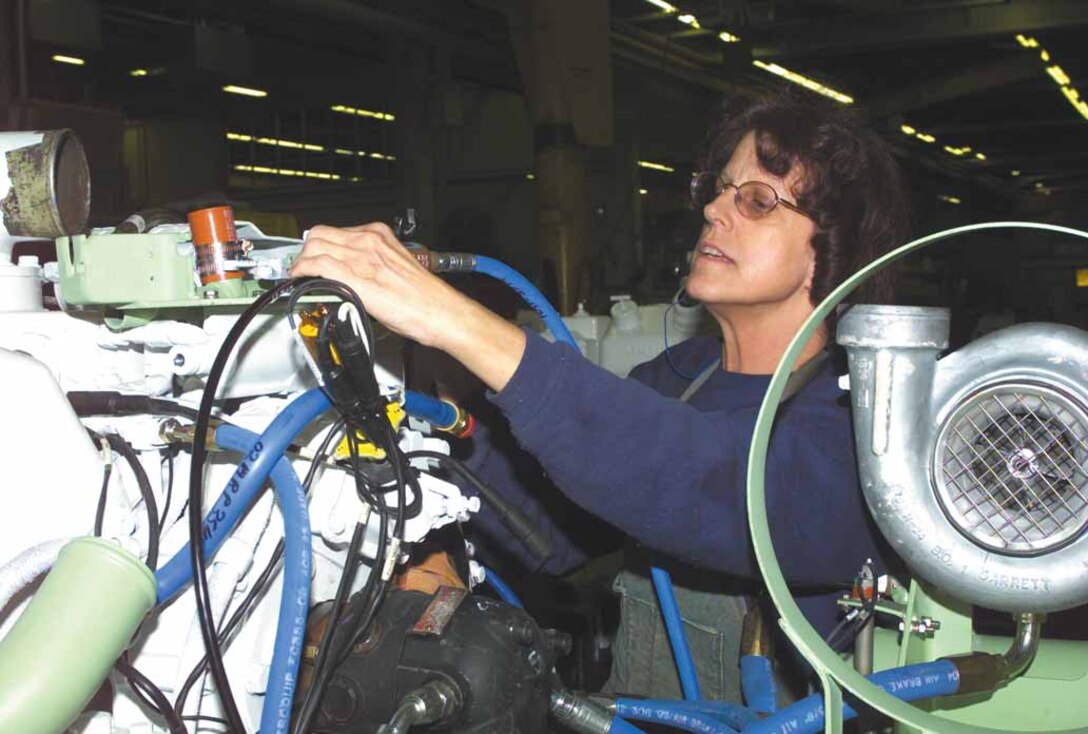 Marsha McClaine, heavy mobile equipment repairer, tightens water and air hoses on a Light Armored Vehicle power pack, which is an engine and transmission combined.