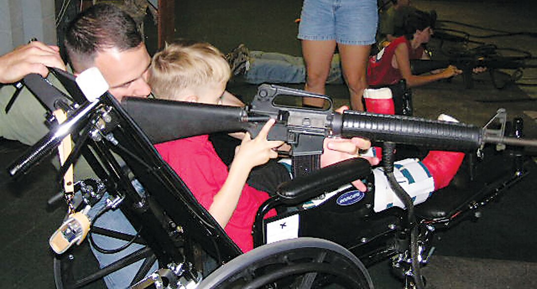 Major Ray Ayer, pilot training officer-in-charge, VMFA-224, MCAS Beaufort, helps his son, Ray, sight in on his target at the Indoor Simulated Marksmanship Training Building aboard the Depot during the Military Parents of Special Needs Children function in June.