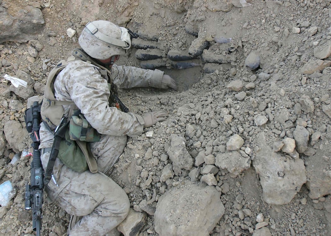 Corporal Matthew G. Coleman, of San Juan, New Mexico, a combat engineer with Battalion Landing Team 1st Bn., 2nd Marines, carefully scoops dirt away from a stack of mortar shells hidden in a rocky hillside by insurgents near Hit, Iraq, Jan. 7, 2006.  The cache was one of several discovered by BLT 1/2 during Operation Hedgehog, the most recent counterinsurgency undertaken by the 22nd Marine Expeditionary Unit (Special Operations Capable) in Iraq.