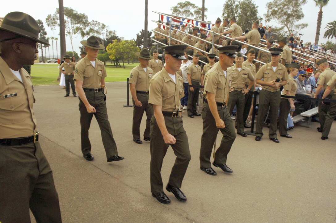 Left, Gunnery Sgt. Michael J. Mullins, drill master, Recruit Training Regiment, looks on as the parade staff from Third Recruit Training Battalion marches onto Shepherd Memorial Drill Field.