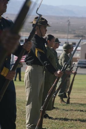 Marines dressed in uniforms of several eras stand at parade rest before the crowd.