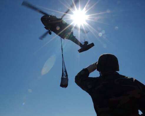 Sergeant Justo Garcia of the 927th CSB from Camp Blanding, Florida observes a UH-60 Blackhawk from B Co. 1st Battalion, 171st Aviation Regiment from Brooksville, Florida as it prepares to drop slingloaded prepackaged food onto the athletic field at Key West Senior High School during Hurricane Wilma Airlift Operations (Florida. Air National Guard photo by Specialist Edouard H.R. Gluch).                     