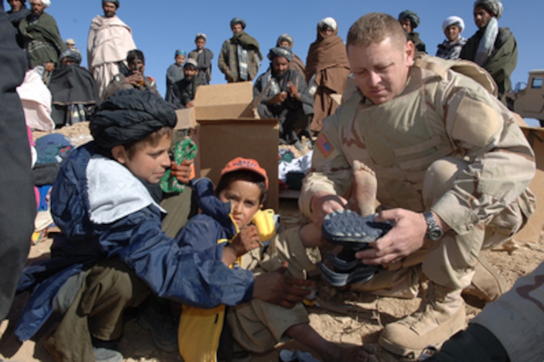 Army Staff Sgt. John Newland helps an Afghan boy try on new boots in Zanto Kalay, Afghanistan, on Jan. 11, 2006. U.S. Army soldiers are bringing medical assistance, donated winter jackets, sweaters, blankets, and food to the people of Zanto Kalay during a medical outreach program. Newland is attached to the Army's 492nd Civil Affairs Battalion. 