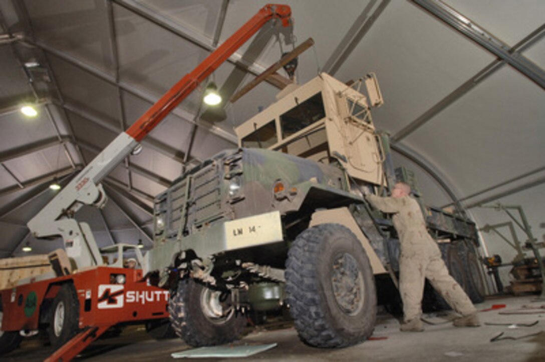 Airman 1st Class Roger Hild, U.S. Air Force, guides the upper portion of an add-on armor kit as it is lowered onto the cab section of an M931 truck tractor at Balad Air Base, Iraq, on Jan. 13, 2006. The add-on armor kit provides the driver and gunner added protection against weapons fire and improvised explosive devices. Hild is deployed to the 732nd Expeditionary Logistics Squadron at Balad Air Base. 