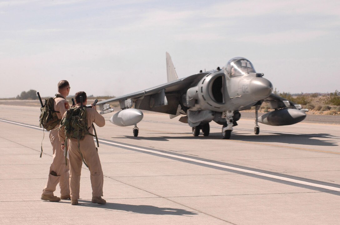 Maj. Eric Austin (left), Marine Attack Squadron 513 executive officer and native of Portland, Ore., and Maj. Guy Berry, VMA-513 maintenance officer and native of Harrisburg, Penn., watch as an AV-8B Harrier II rolls past after making a landing on echo taxiway Jan. 26. VMA-513 is deploying to Iraq soon, so they practiced landing on echo taxiway in case they will need to land on surfaces smaller than the runways available on station.
