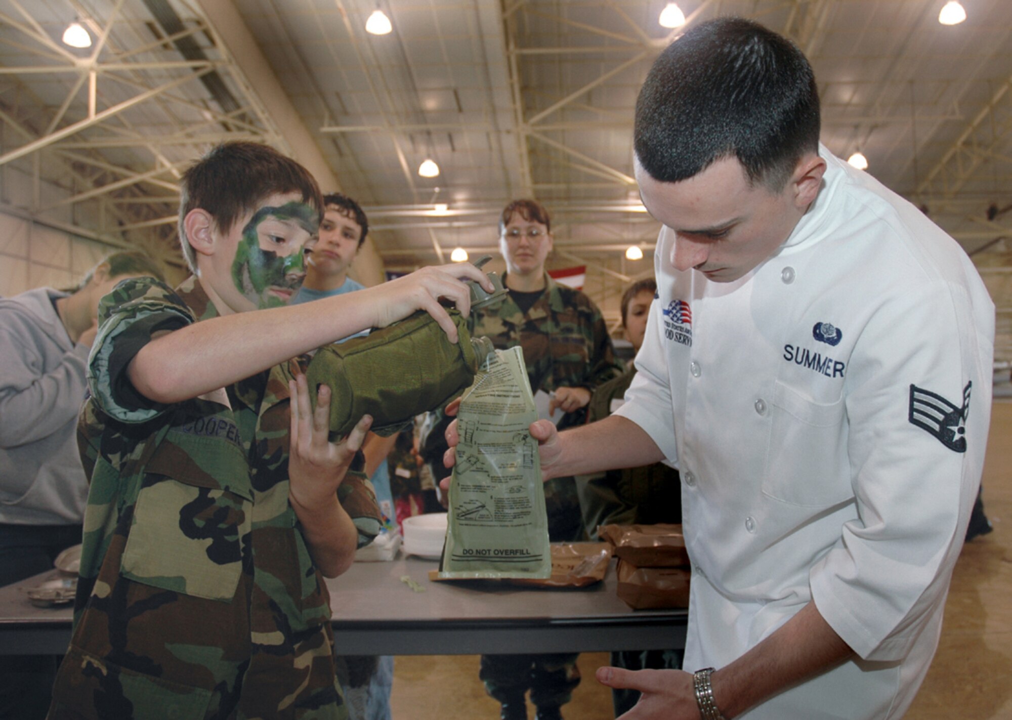 TYNDALL AIR FORCE BASE, Fla. (AFPN) -- Trent Frey pours canteen water into a Meals, Ready to Eat heating container with the help of Senior Airman Jon Summer of the 325th Services Squadron. (U.S. Air Force photo by Chrissy Cuttita)
