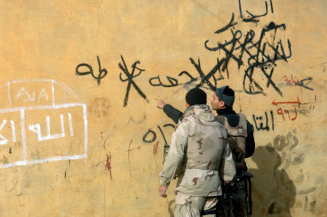 A U.S. Army soldier listens as an Iraqi interpreter explains the anti-American graffiti scrawled on a wall in the city of Bi'aj, Iraq, on Jan. 26, 2006. Soldiers from the 1st Battalion, 3rd Armored Combat Regiment are conducting cordon and search operations in the city. 