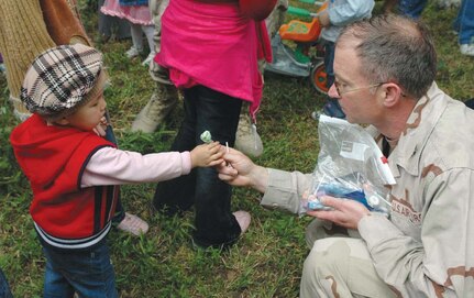Col. Frederick Schaefer, 376th Expeditionary Medical Group commander deployed from Elmendorf, gives a child candy during the Manas Village Children’s Day celebrations.