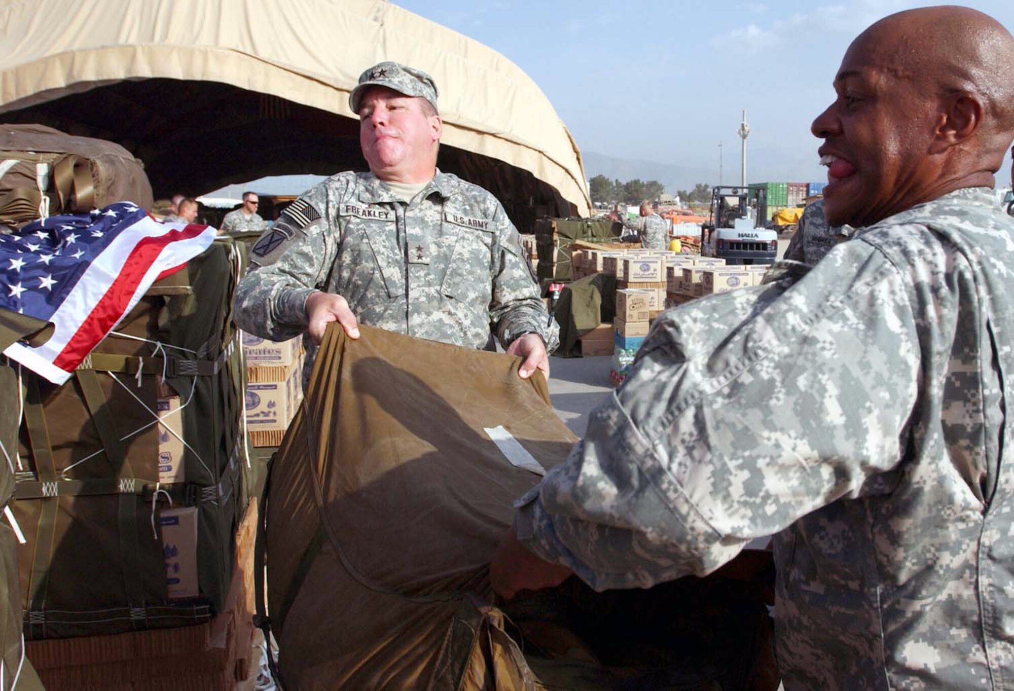 Army Maj. Gen. Benjamin C. Freakley (left) and Army Col. Larry D. Wyche lift a parachute on top of an aerial delivery bundle on Monday, July 3, at Bagram Air Field, Afghanistan. They along with other senior leaders helped prepare special Independence Day bundles that were airdropped to Soldiers at forward operating bases throughout Afghanistan by aircrews from the 774th Expeditionary Airlift Squadron on the Fourth of July. The bundles contained items such as soda, beef jerky, CDs and DVDs requested by Soldiers to enhance morale. General Freakley is the commander of Combined Joint Task Force-76, and Colonel Wyche is the commander of the Joint Logistics Command. (U.S. Army photo/Sgt. 1st Class Michael Rautio)