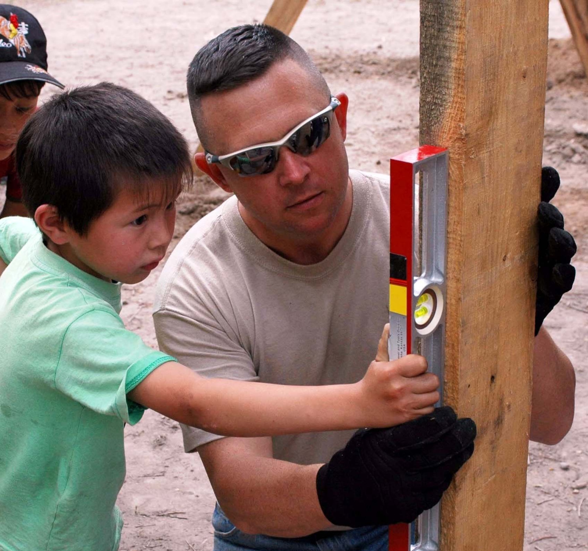 Tech Sgt. William Gordon, 376th Expeditionary Security Forces Squadron, shows an Oktobersky Village School student how to level a wood plank. Members of the 376 SFS and 376th Civil Engineer Squadron began construction on the playground in May. Sergeant Gordon is deployed from the 482nd Security Forces Squadron, Homestead ARB, Fla. (US Air Force photo by Staff Sgt. Candy Knight)