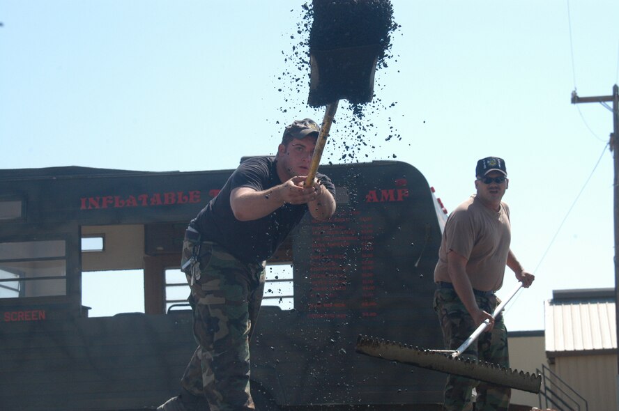 Senior Airman Michael MacMillan, 7th CES equipment operator, and Tech. Sgt. Jason Falkenstein, 7th CES Dirt Boyz supervisor, hurl hot asphalt onto an area that was then steamrolled and set on base July 14.                                
