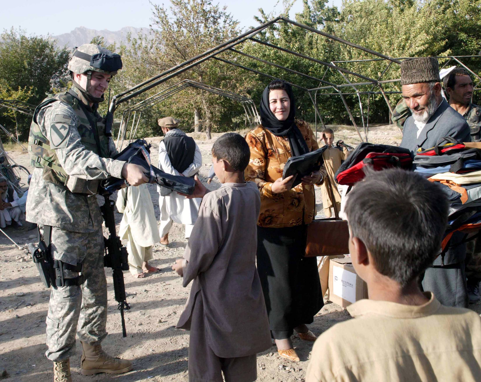 Army Sgt. Levi Dahlstrom and Aziz Sedat hand out new backpacks and school supplies on July 19 to children from seven villages affected by the arsonists who burned tents that housed their school at Nyazi Geranshakh in the Parwan Province of Afghanistan. Sergeant Dahlstrom is a member of the civil affairs team and Ms. Sedat is the Parwan director of education. (U.S. Air Force photo/Capt. Mark Gibson)