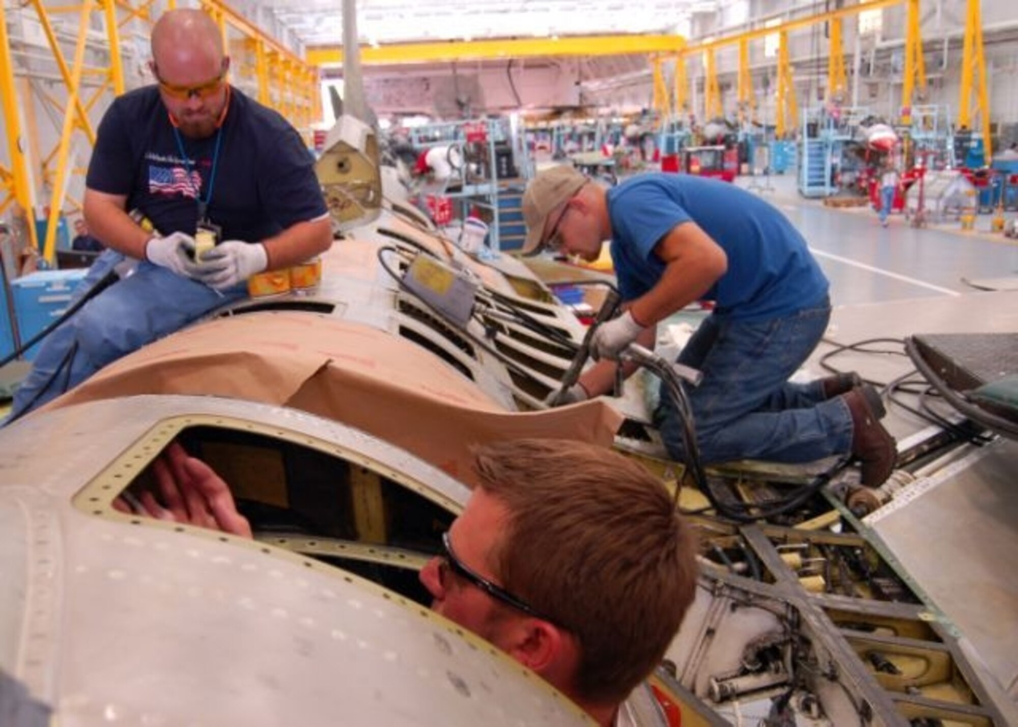 HILL AIR FORCE BASE, Utah — Steve Vanballegooie, an aircraft pneudraulics systems mechanic with the 573rd Aircraft Maintenance Squadron, laces up the F-1 bladder cell of an F-16 while crammed into a 10x10 square foot work space. Mr. Vanballegooie  said it’ll take about two days to complete. At right, Jordan Smith, and at left, Brodie Martin, both sheet metal mechanics with the 573rd AMS, fix fastener holes on the F-16’s “turtle back.” The turtle back houses hydraulics and fuel lines; the work part of Falcon STAR – a structural modifications program that will take the service life of the aircraft to the year 2020. The F-16 customer is the Burlington Air National Guard in Vermont. (Air Force photo by G. A. Volb)  