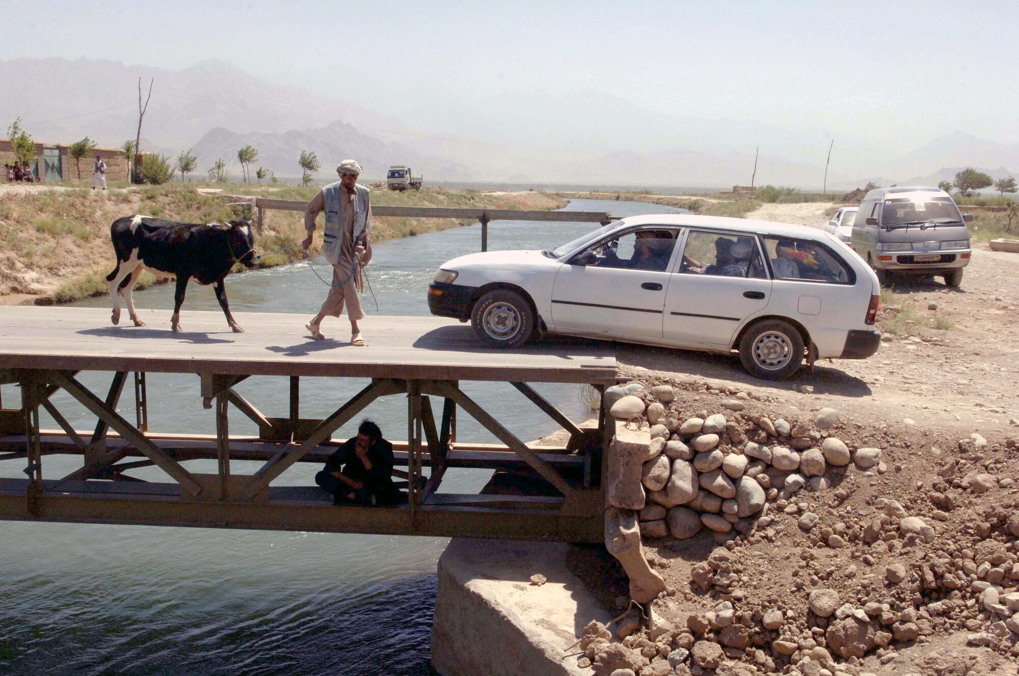 JABAL SARAJ, Afghanistan -- A car driver has to wait for a man and his cow to cross the bridge before he can cross. The Bagram Provincial Reconstruction Team helped improve a road and build a two-way bridge here.