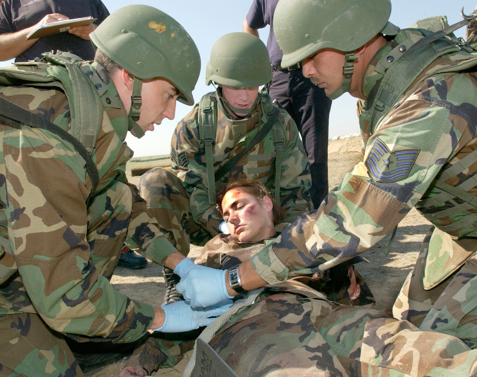 Capt. Kevin James (left), Staff Sgt. Michael Johns (center), and Tech. Sgt. Robert Norris (right), 2nd Space Warning Squadron assist the "victim" Staff Sgt. Lisa Harmon, 460th Medical Group, during the Self Aid and Buddy Care competition held at Camp Rattlesnake July 13. Sergeant Harmon had "suffered" multiple wounds from a simulated mortar explosion. Enduring 100-degree weather, teams representing various units in the 460th Space Wing competed in the practical test and obstacle course carrying a 155 pound dummy on a stretcher. (Air Force photo by Staff Sgt. Chenzira Mallory)