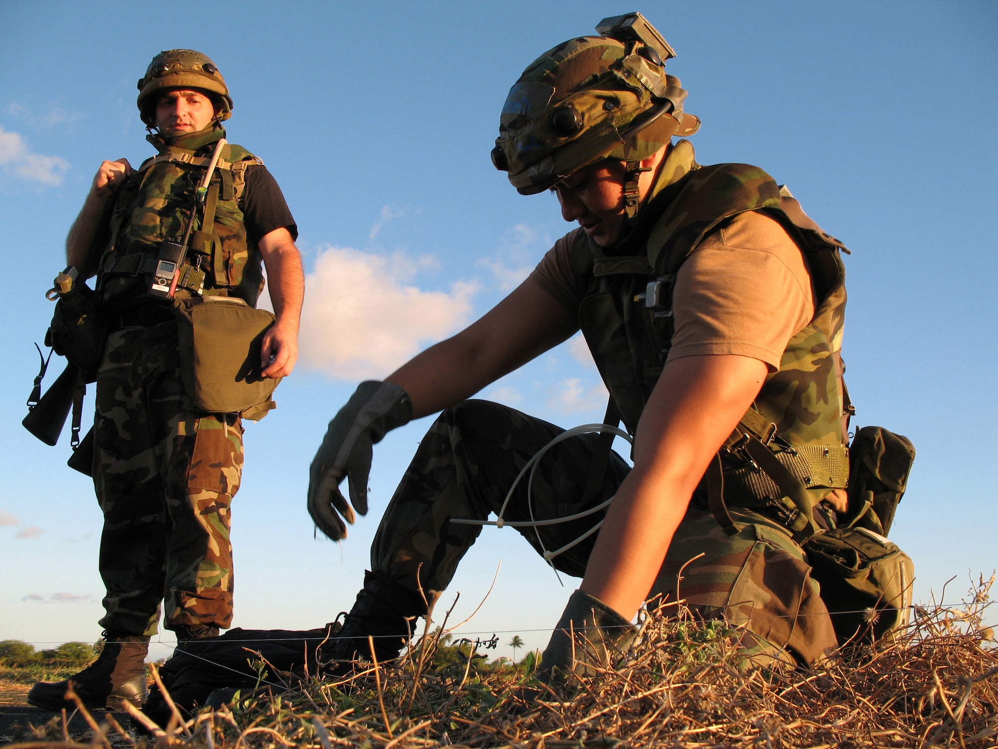 Chief Master Sgt. William Stumbo Jr. watches as Senior Airman Julius Valenzuela sets glow stick traps to warn of enemy intrusions during an exercise at Naval Station Barber's Point, Hawaii, on July 25. They are with the Hawaii Air National Guard's 297th Air Traffic Control Squadron. (U.S. Air Force photo/Tech. Sgt. Chris Vadnais)
