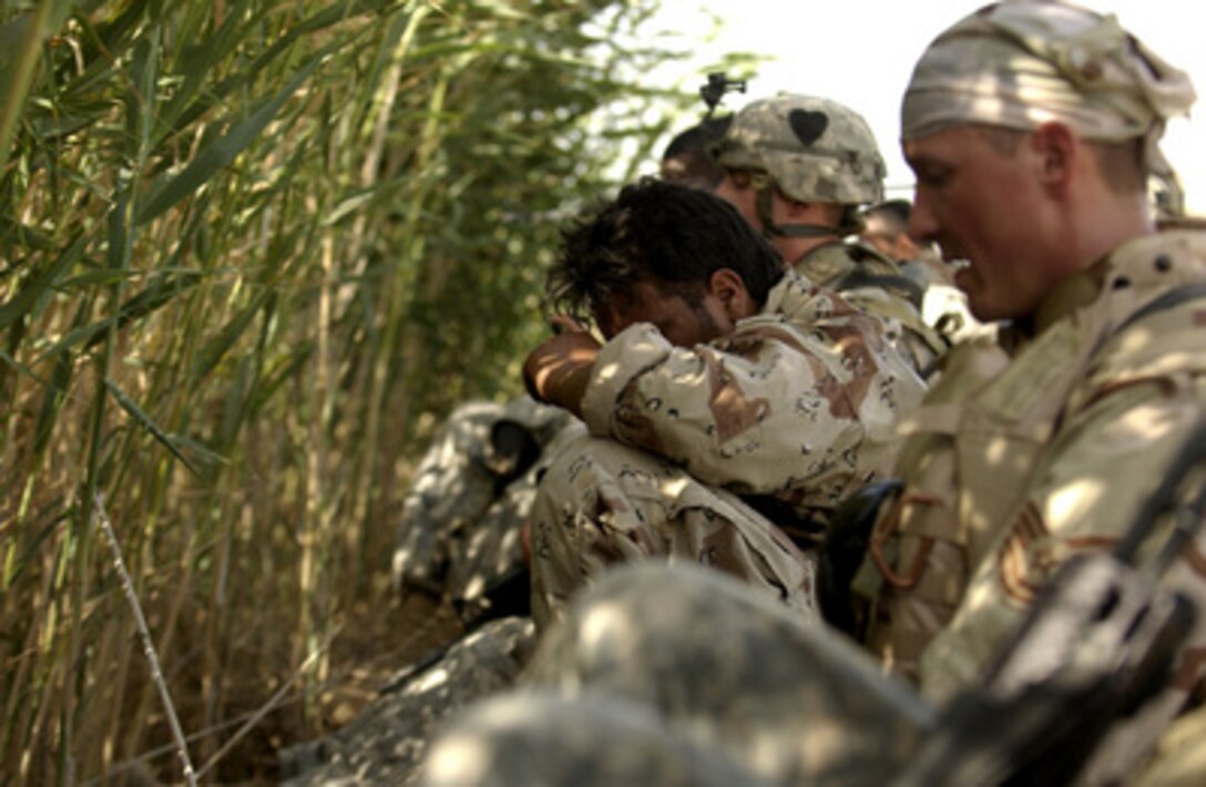 U.S. Army soldiers, Air Force airmen and Iraqi army soldiers take a break from the heat in the shade of some rushes while searching for weapons caches and improvised explosive devices in Yusufiyah, Iraq, on June 1, 2006. The troops in Iraq have been working in temperatures over 100 degrees Fahrenheit. 