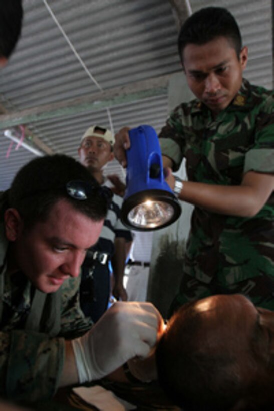 U.S. Navy Hospital Corpsman Taylor Simpkins (left) removes stitches from a man's head as an Indonesian soldier holds a flashlight at the Global Rescue Network's mobile hospital in Jetis, Indonesia, on June 3, 2006. The man received injuries when the ceiling of his home collapsed during a magnitude-6.2 earthquake that devastated central Indonesia on May 27, 2006. 