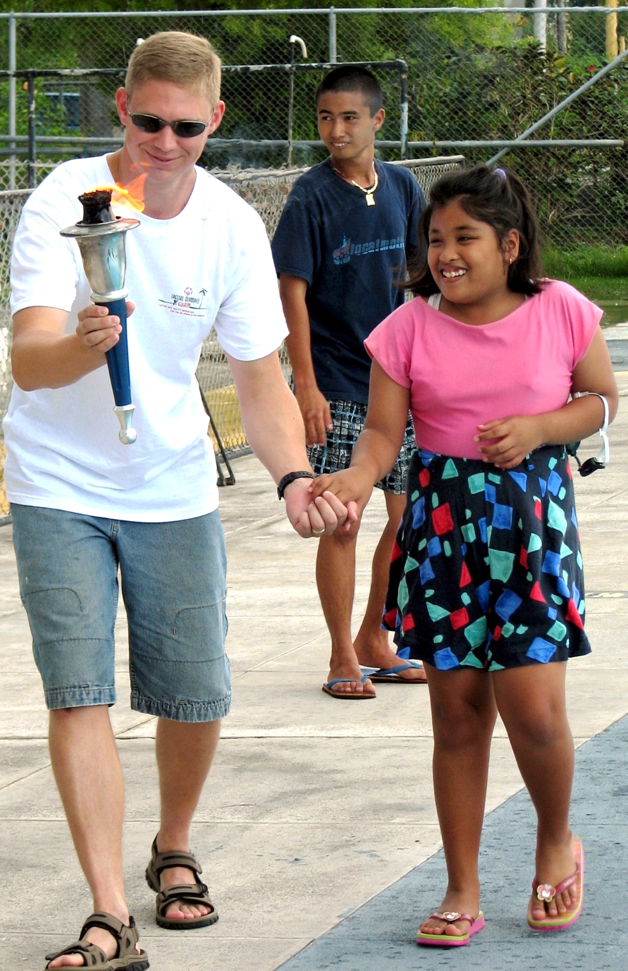 Capt. Ryan Huckabay holds the hand of athlete Miah Meneses while carrying the torch at the opening ceremonies of the 2006 Guam Special Olympics aquatic event on Saturday, June 3, 2006. Volunteers from the 393rd Expeditionary Bomb Squadron and 36th Expeditionary Aircraft Maintenance Squadron at Andersen Air Force Base, Guam, assisted at the events, acting as official timekeepers, distributing medals and helping in other areas. Captain Huckabay is assigned to the 393rd EBS. (U.S. Air Force photo/Tech. Sgt. Mikal Canfield)