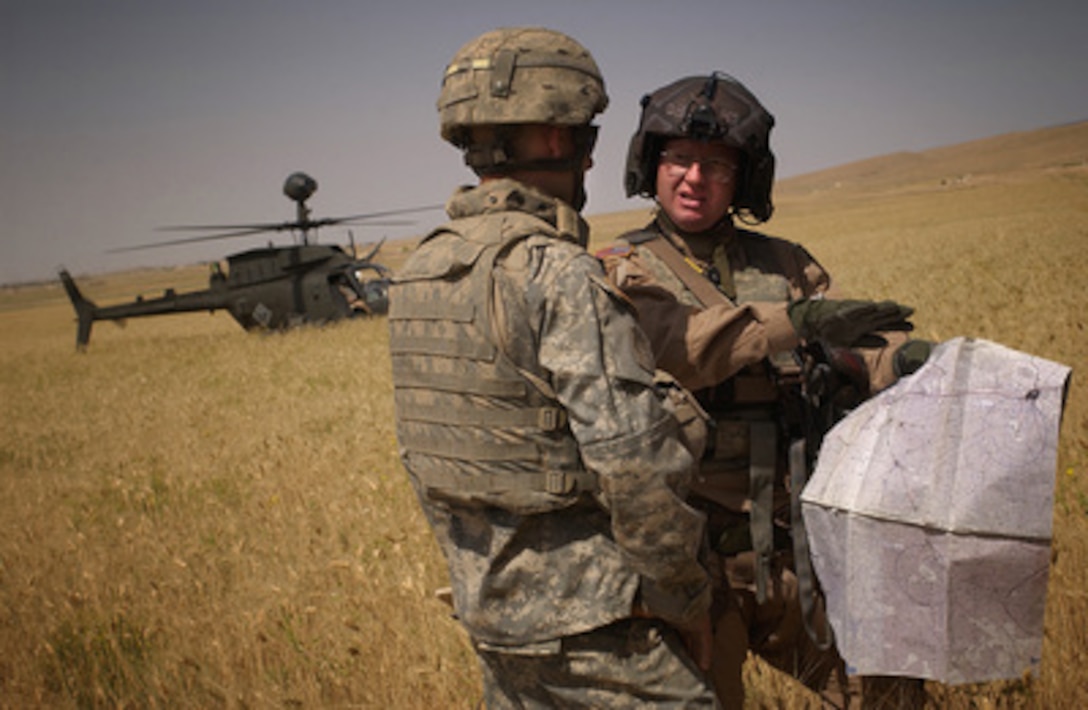 U.S. Army 1st Lt. Paul Laborde (left) talks with the pilot of an OH-58 Kiowa Warrior helicopter in a field near Sinjar, Iraq, during a search for weapons caches on May 31, 2006. Laborde and other soldiers of the 4th Battalion, 14th Cavalry Regiment, 172nd Stryker Brigade Combat Team are working in concert with the helicopter crew to search for hidden weapons. 