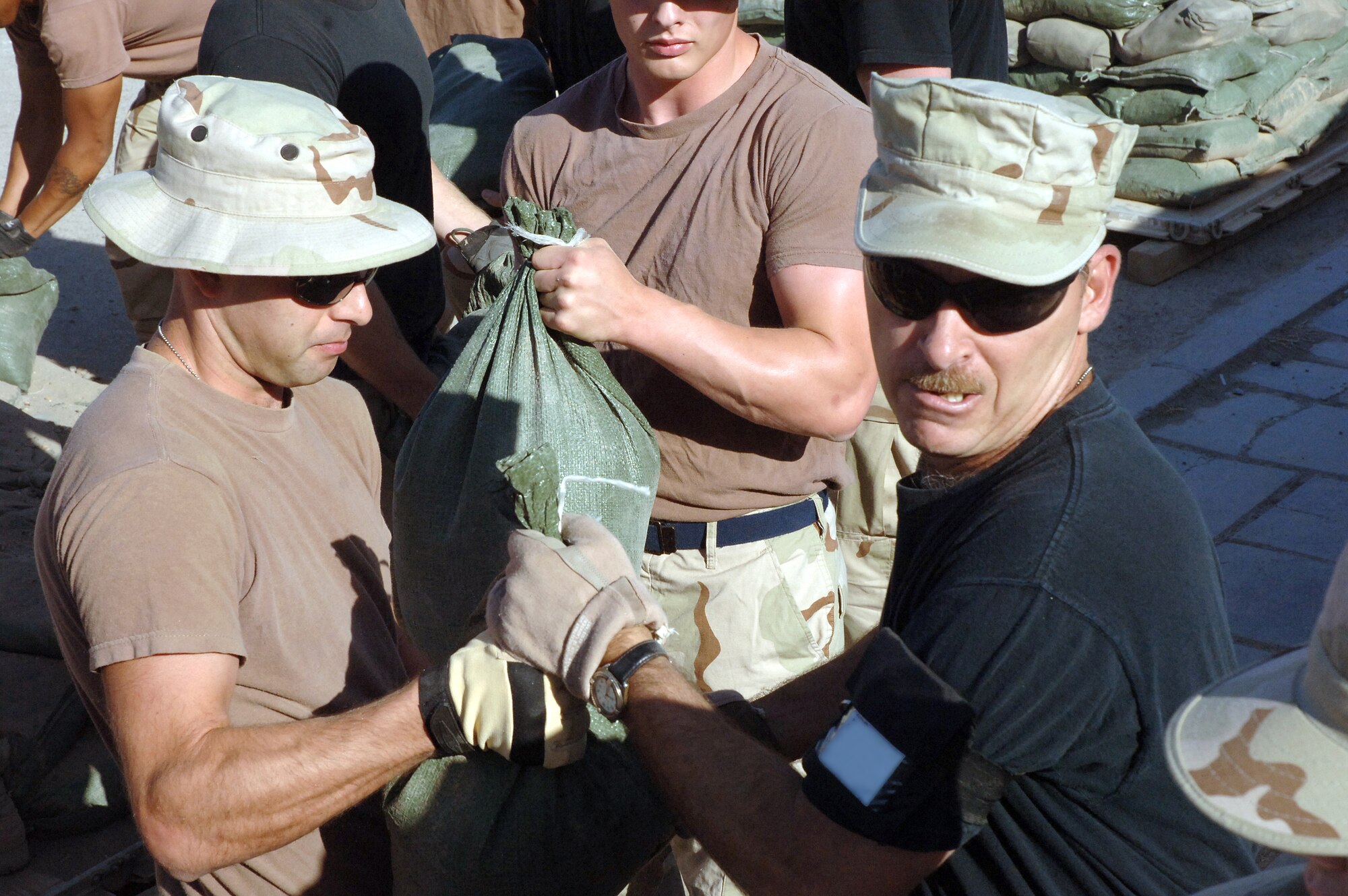 Tech. Sgt. Tonay Bonanno (left) passes a sandbag to Master Sgt. Stephen Runyan as Airmen from the 447th Air Expeditionary Group perform a "bucket brigade" to reinforce the sides of the recreation tent at Sather Air Base, Iraq, on Wednesday, June 7, 2006. More than 50 Airmen from the 447th AEG teamed up to sandbag their recreation tent in order to keep the cool air inside from escaping. Sergeants Bonanno and Runyan are deployed from the 96th Services Squadron at Eglin Air Force Base, Fla. (U.S. Air Force photo/Staff Sgt. Bryan Bouchard) 