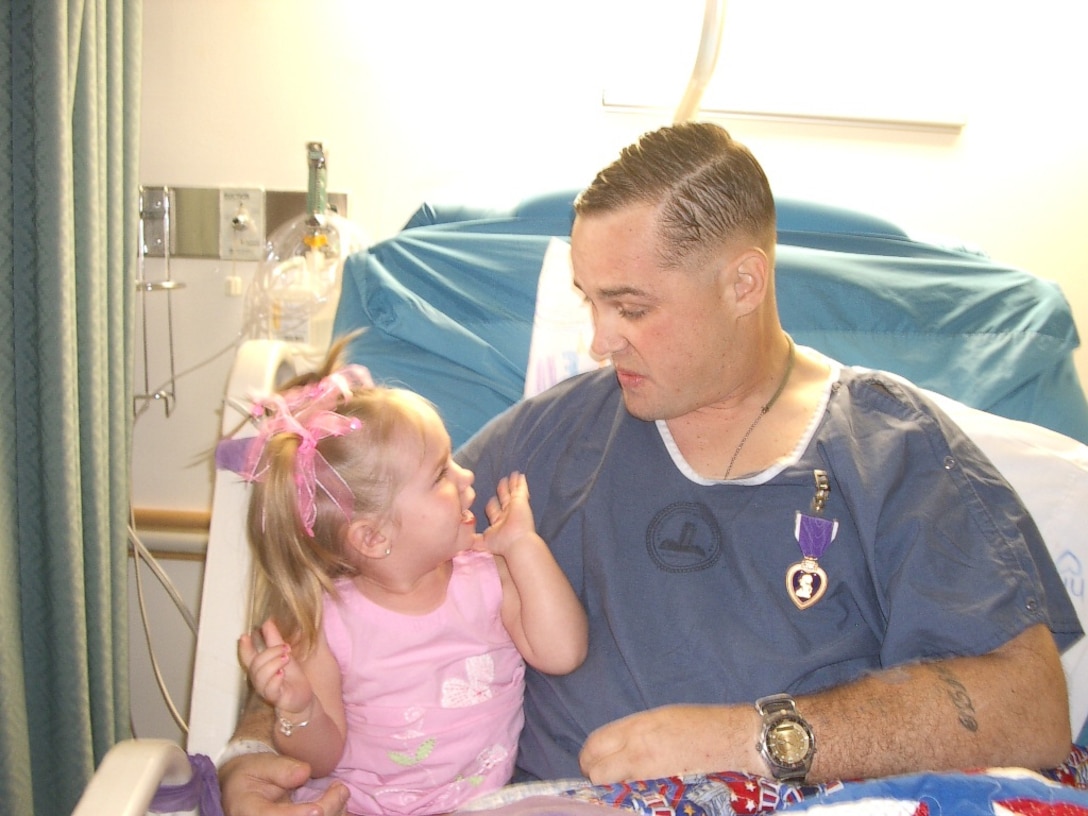 Master Sgt. William 'Spanky' Gibson, force fires chief, Multi National Force - West, and holds his daughter Lauren after being awarded the Purple Heart at Bethesda Naval Hospital, Md., june 9, 2006.  Gibson, an above-the-knee amputee from Pryor, Okla., was recently selected as one of three Marine Corps staff non-commissioned officers for the first ever Marine staff NCO Congressional Fellowship.  Gibson lost his left after being shot by a sniper in Ramadi, Iraq, May, 2006.  He was serving as a joint termina attack controller for 1st Air Naval Gunfire Liaison Company.