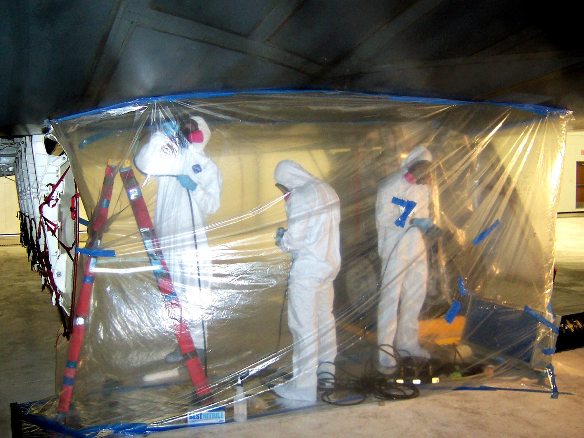 Airmen with the 36th Expeditionary Aircraft Maintenance Squadron sand off degraded paint coatings on a B-2 Spirit bomber at Andersen Air Force Base, Guam. The aircraft was restored once new paint coatings were applied. The plastic tent is used to contain the sanding dust created while removing the paint coatings. (U.S. Air Force photo/Maj. Kelly Scott) 
