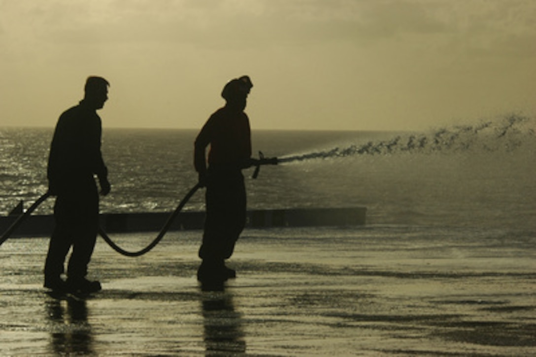 U.S. Navy Petty Officer 3rd Class Scott Bosboe (left) and Airman Charles Mackabee conduct a salt water wash down aboard the aircraft carrier USS Kitty Hawk (CV 63) on June 13, 2006. 