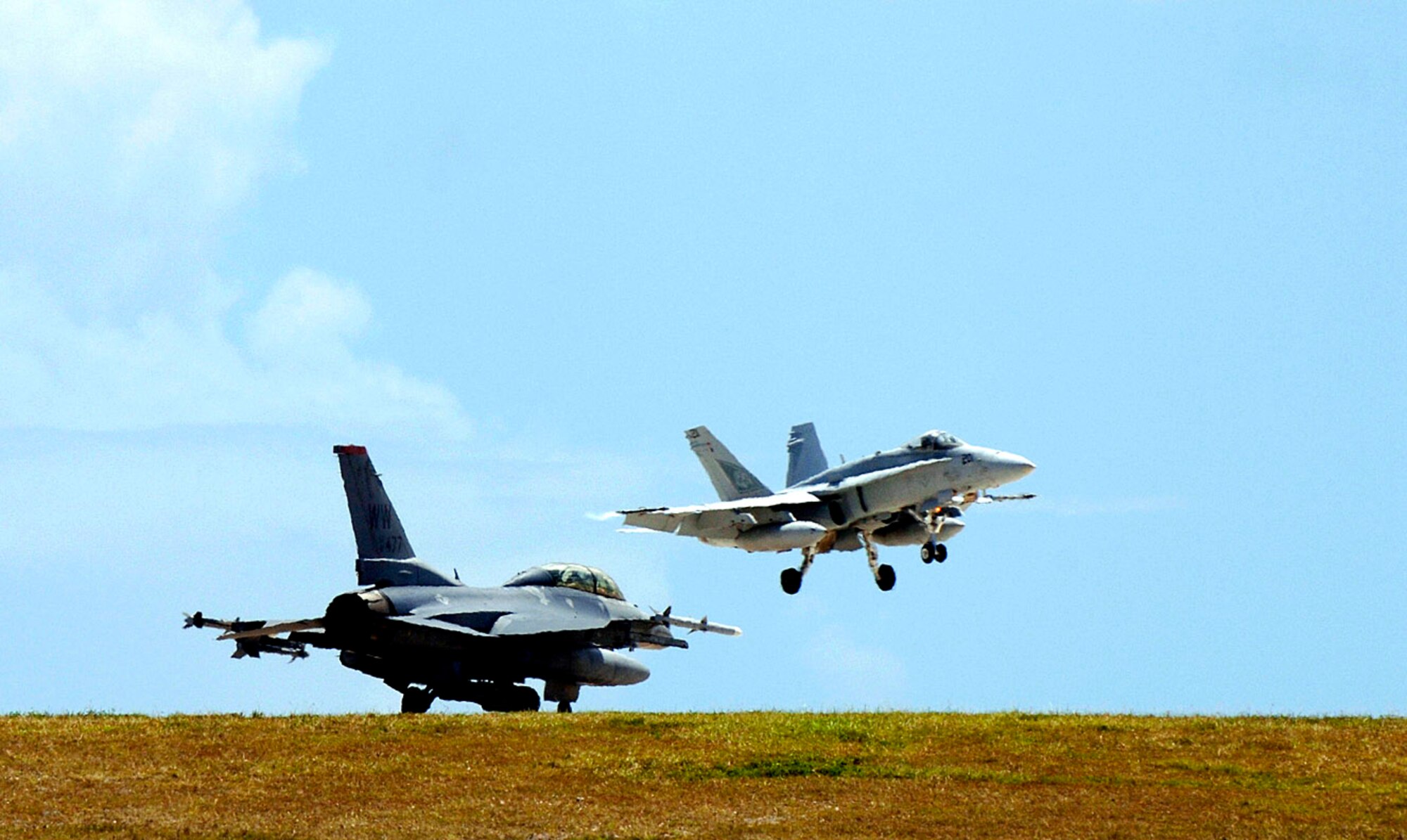 An F-18 Hornet prepares to land while an F-16 Fighting Falcon awaits clearance to take off for a training sortie at Andersen Air Force Base, Guam, as part of Exercise Valiant Shield 2006 on Monday, June 19. Valiant Shield, a U.S. Pacific Command exercise, runs June 19 to 23. It focuses on integrated joint training and interoperability among U.S. military forces while responding to a range of mission scenarios. (U.S. Air Force photo/Staff Sgt. Bennie J. Davis III)